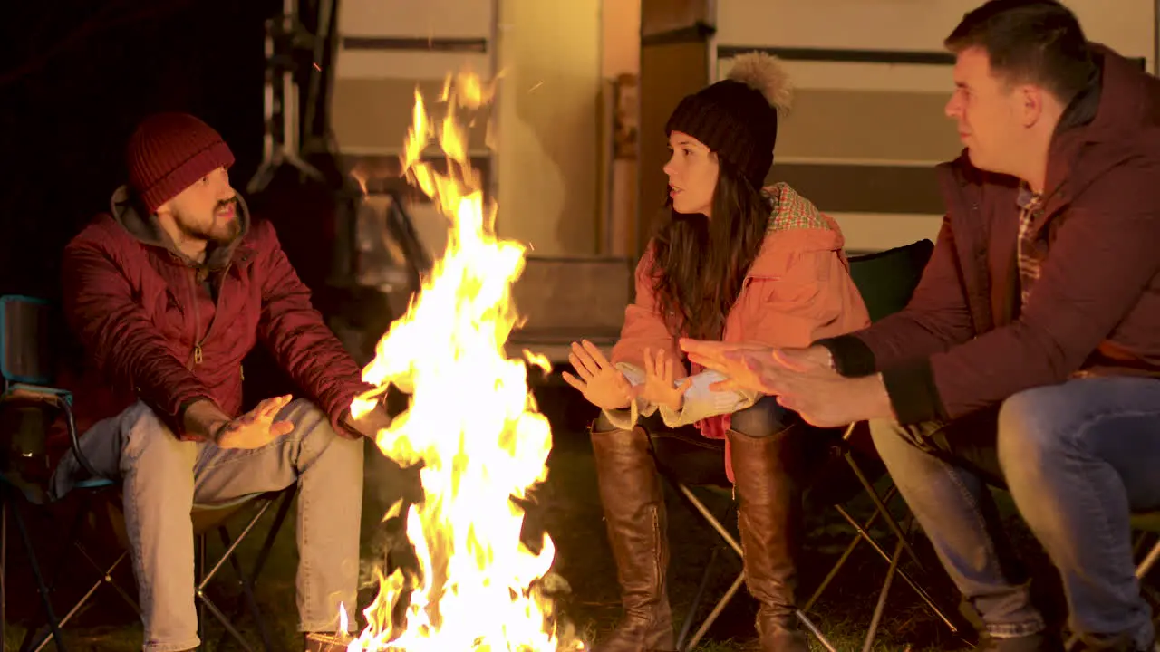 Handheld footage of friends warming their hand at camp fire in a cold autumn night