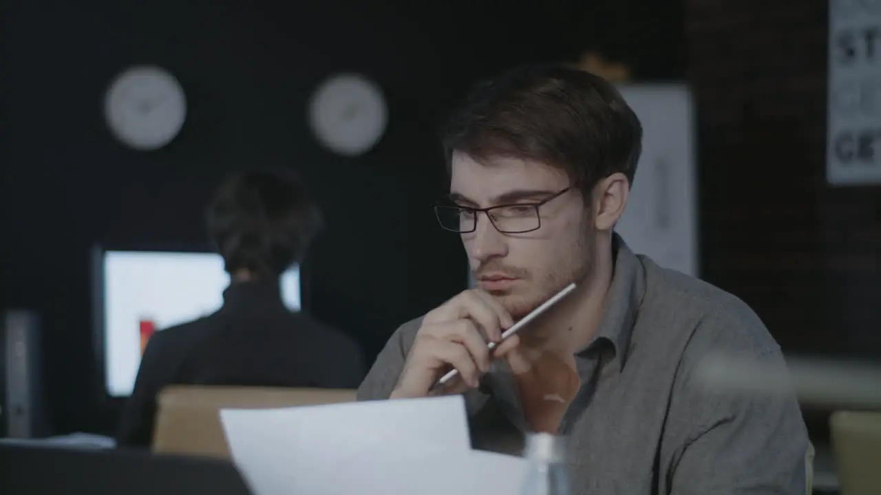 Concentrated business analyst watching document and laptop screen in dark office