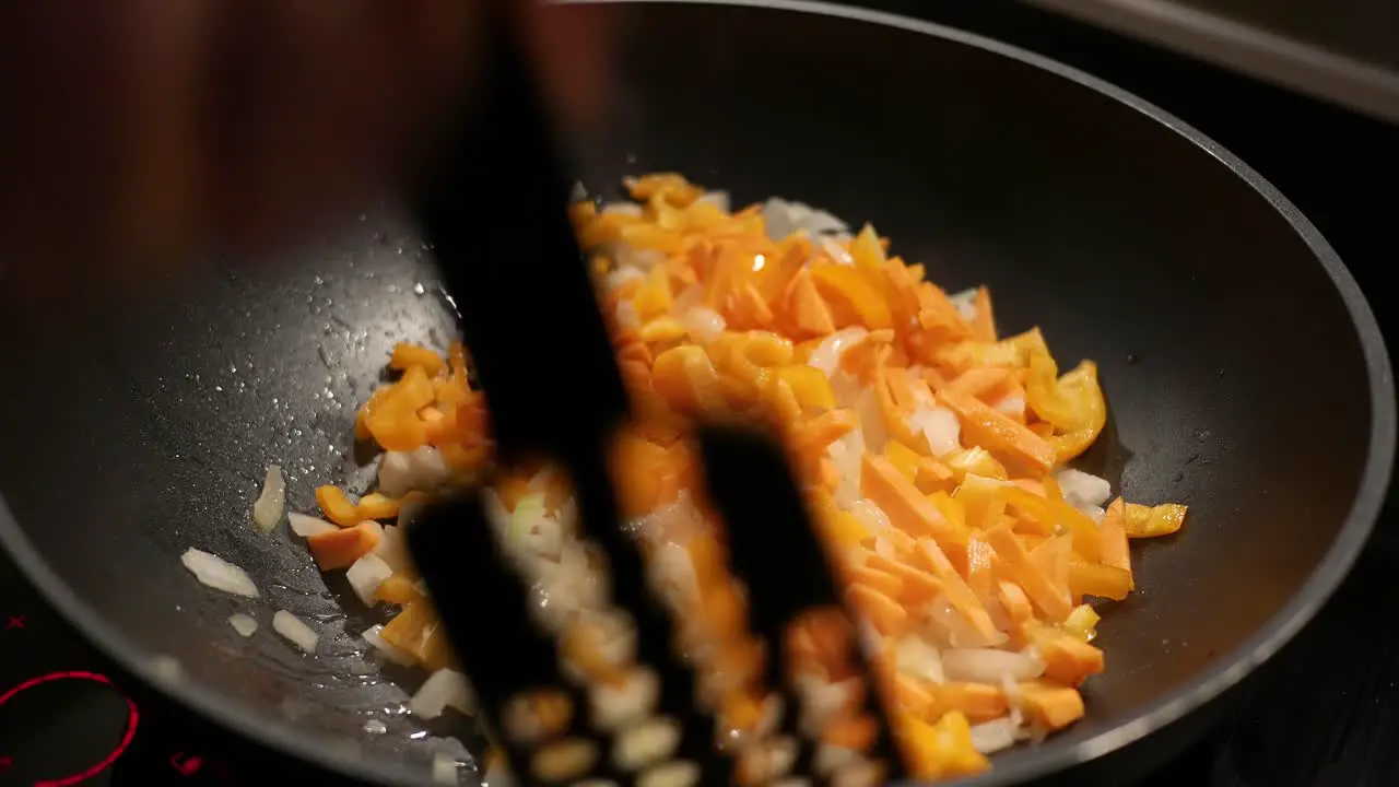 A female hand mixes finely chopped onions and carrots in a pan