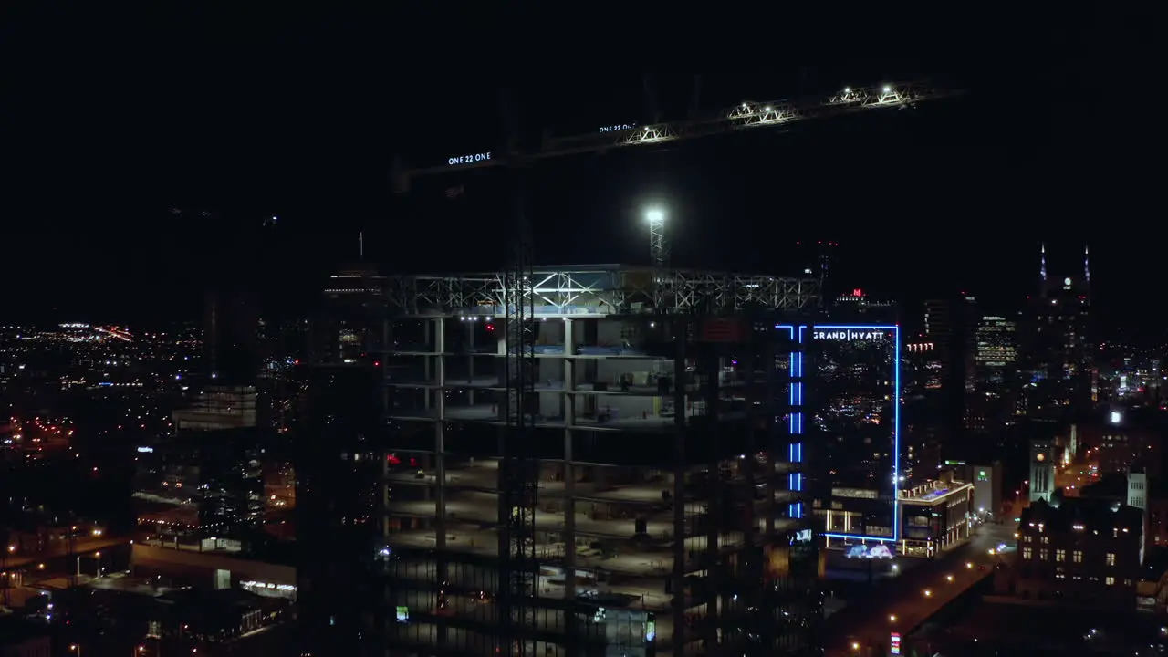 Ascending night aerial up tower under construction with cranes in city 4K