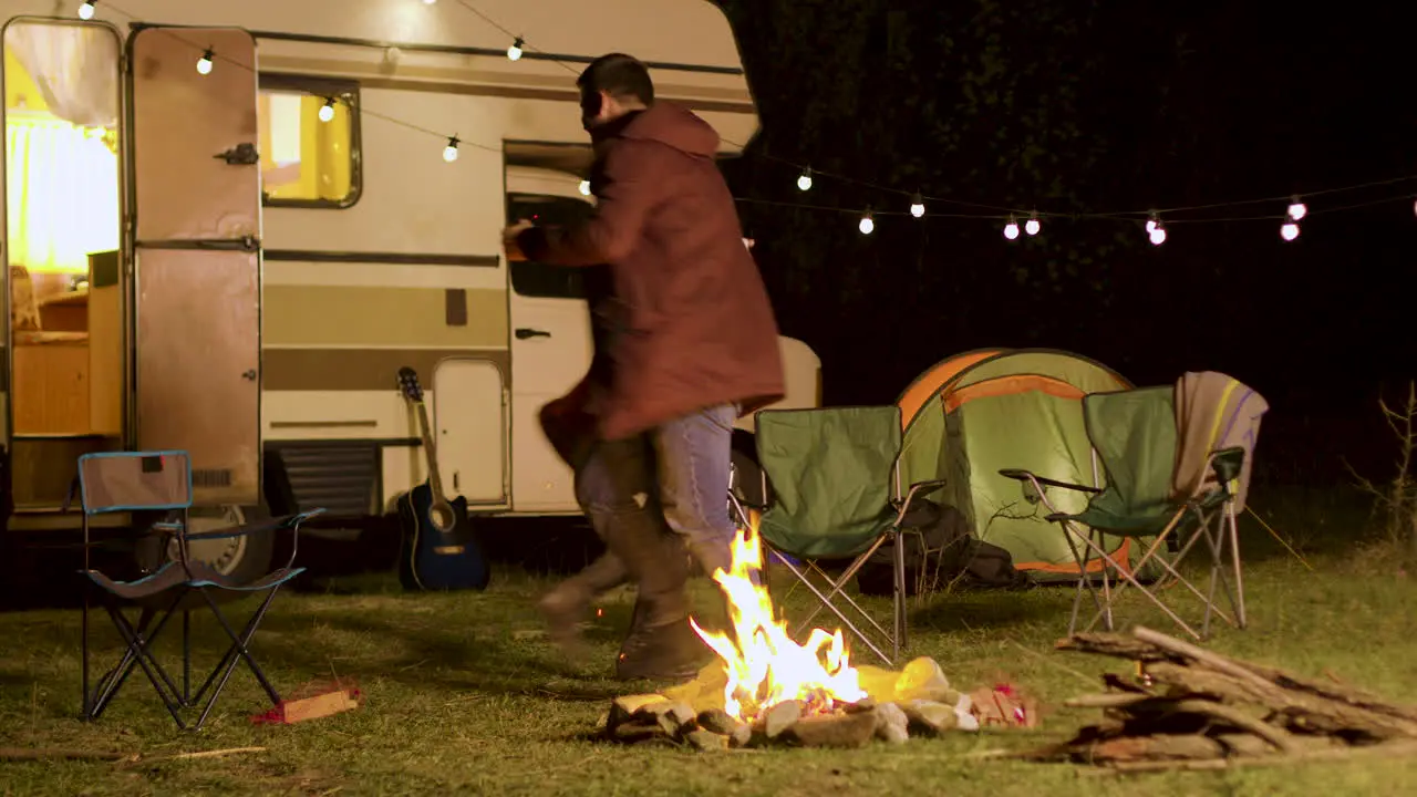 Cheerful young couple dancing around camp fire in cold night of autumn