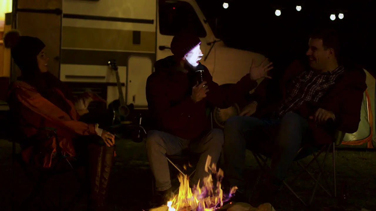 Bearded man telling a scary story to his friends around camp fire