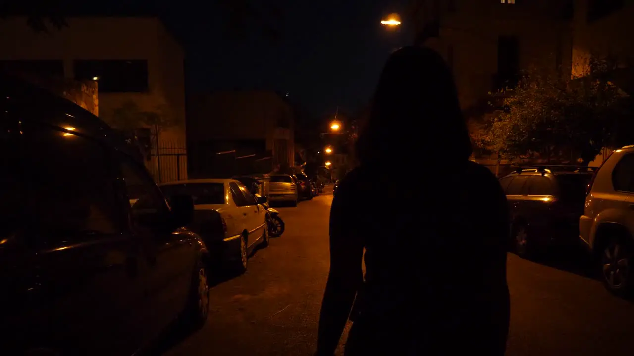 Night shot of a woman walking down a road with parked cars on both sides