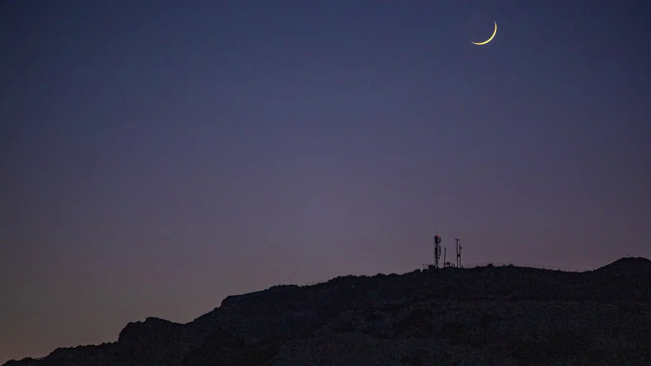 Timelapse of the crescent moon in motion at night over a mountain