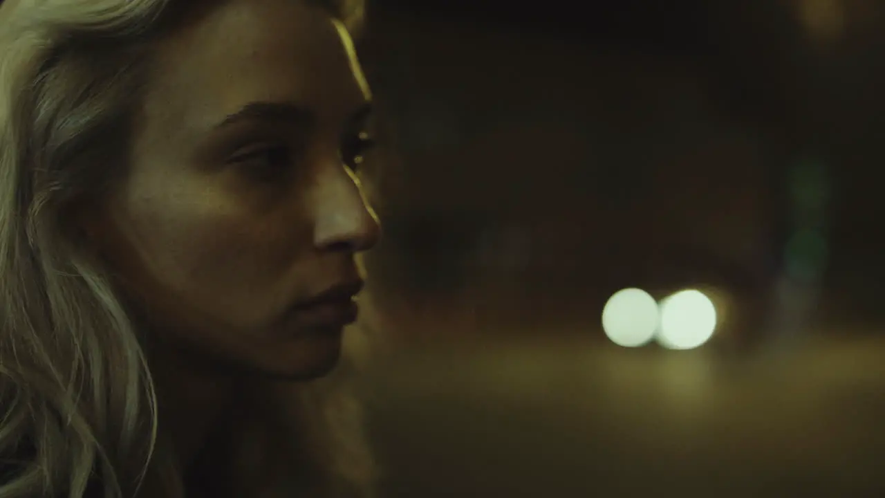 Blonde woman city night face looking at cars passing in street lights