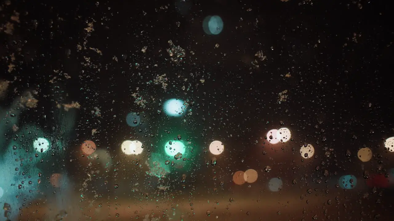 Snowflakes falling on the window melting blurred city lights in the background