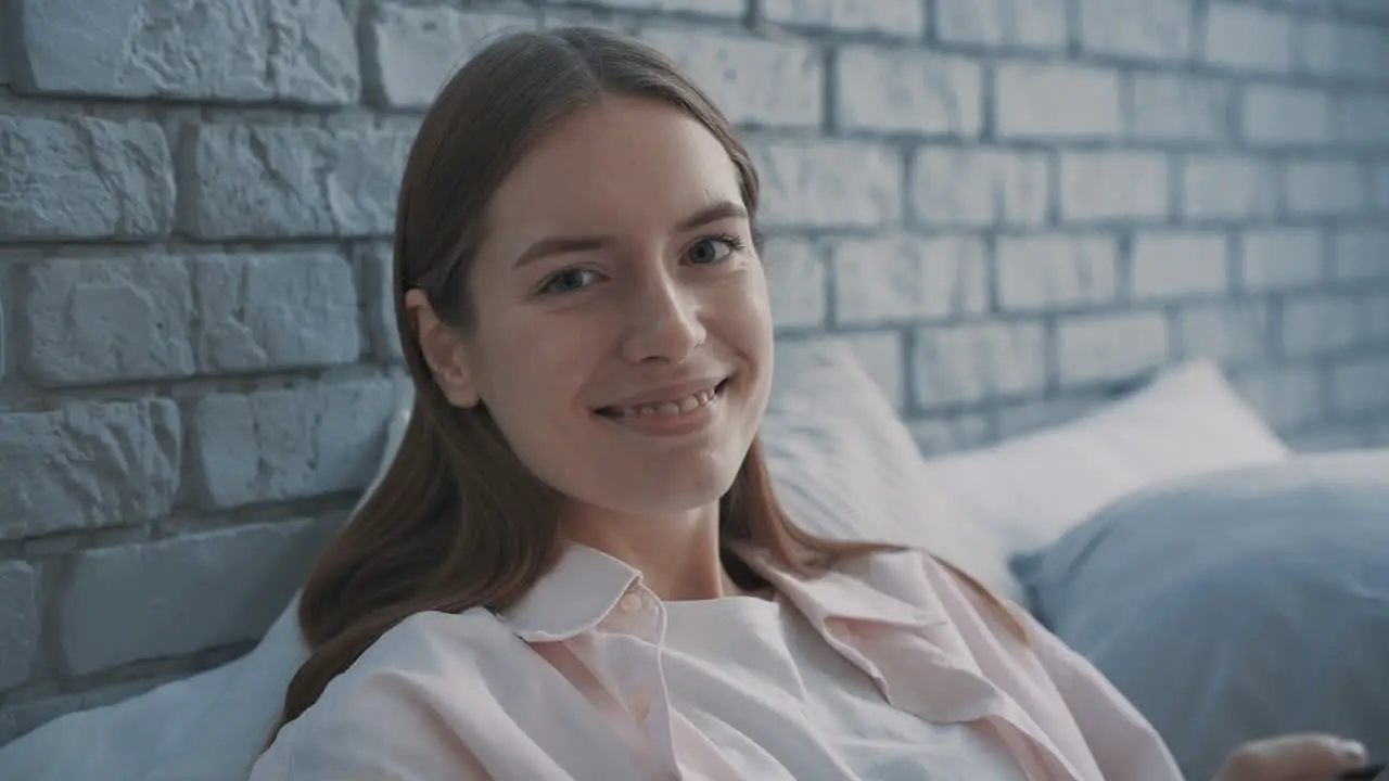 Retrato De Una Joven Mujer Bonita Sonriendo Y Mirando A La Cámara Sentada En La Cama Interior