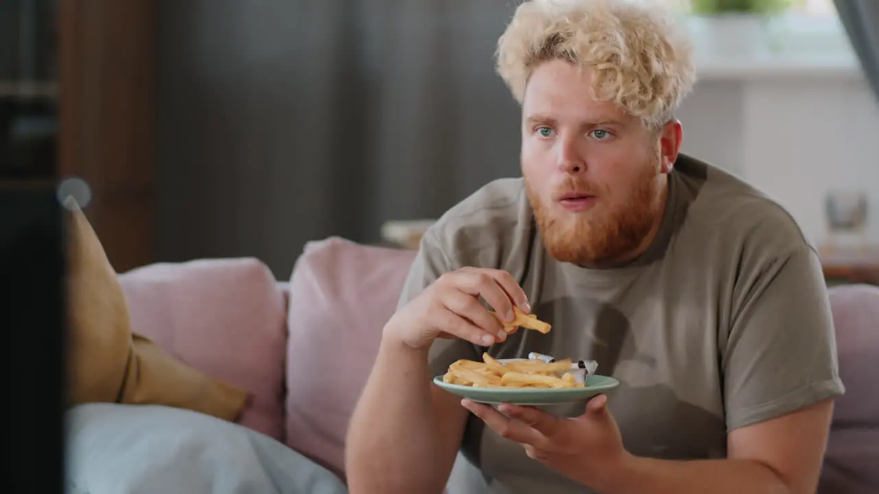 Hombre Obeso Comiendo Papas Fritas Con Ketchup Mientras Ve La Televisión En Casa