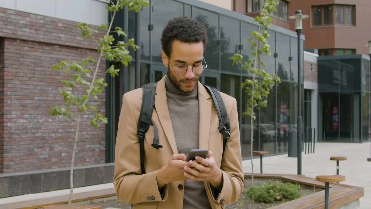 Hombre Americano Sonriente Con Ropa Formal Usando Teléfono Móvil Y Mirando A Su Alrededor Mientras Está De Pie Con Su Bicicleta En La Calle