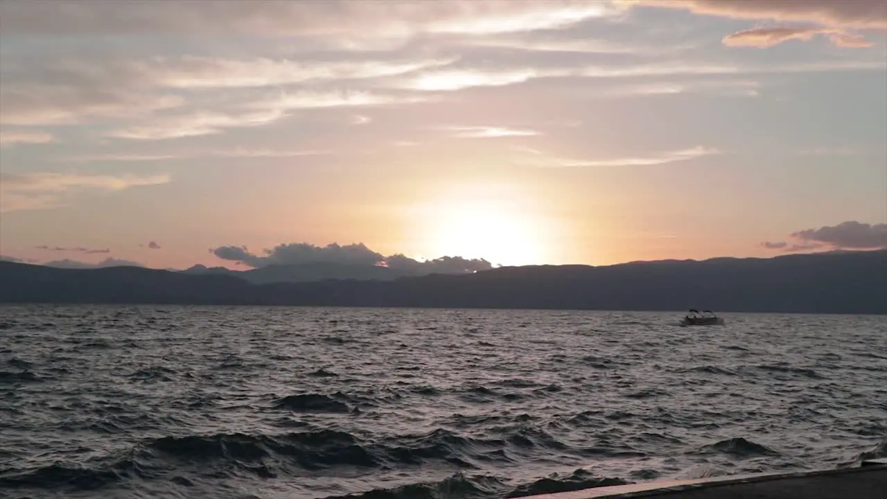 Small boat travelling on water in a windy stormy lake at sunset