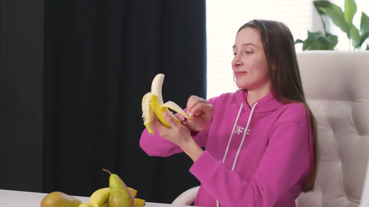 Mujer Joven Feliz Sentada En El Escritorio Pelando Y Comiendo Plátano