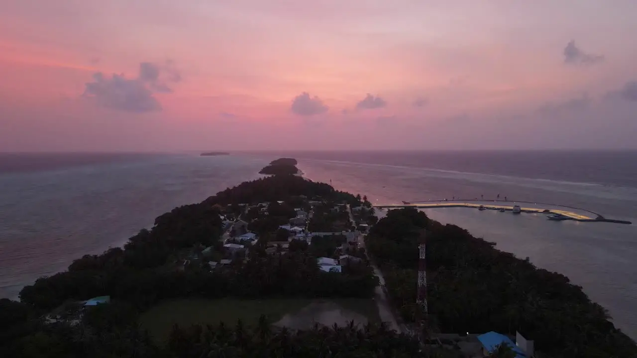 Magical drone shot after sunset in Maldives flying over an island with clouds in the distance and pink sky