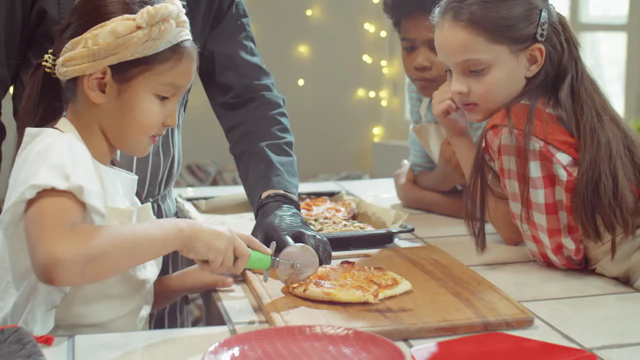 Kleines Asiatisches Mädchen Das Pizza Beim Koch-Meisterkurs Schneidet