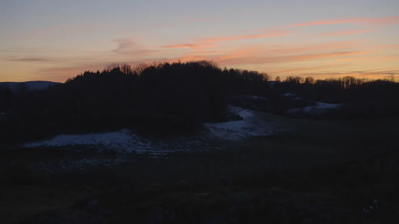 Calm sunset with pastel-like colours behind a meadow slow tilt up handheld