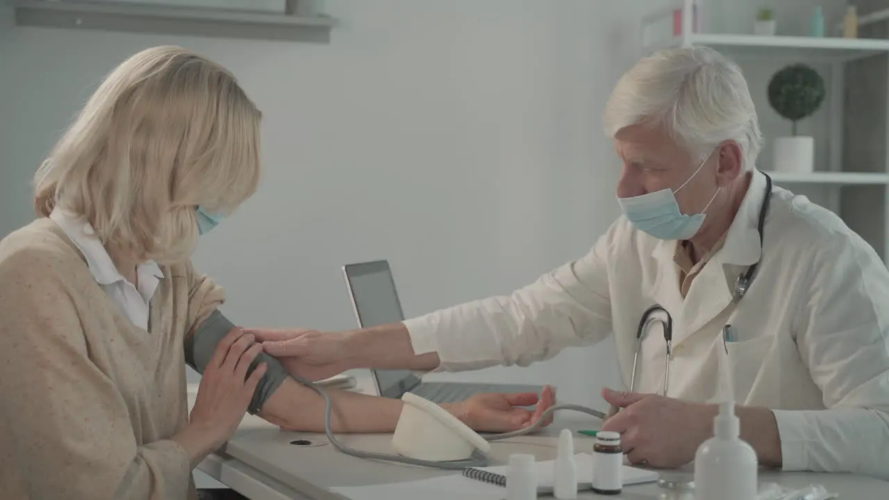 Ein Grauhaariger Arzt Mittleren Alters In Einer Gesichtsmaske Nimmt Einer Patientin Den Blutdruck