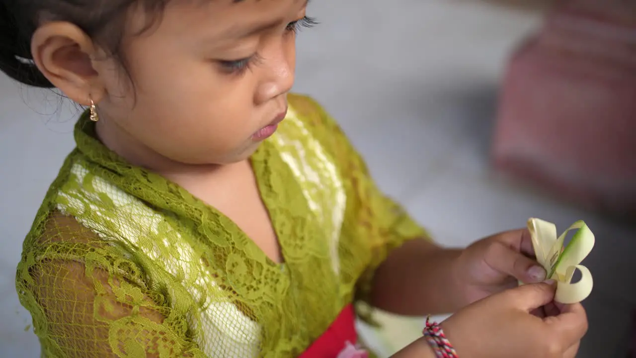 Pretty Asian child folds strips of leaves into a design and staples the pieces in place