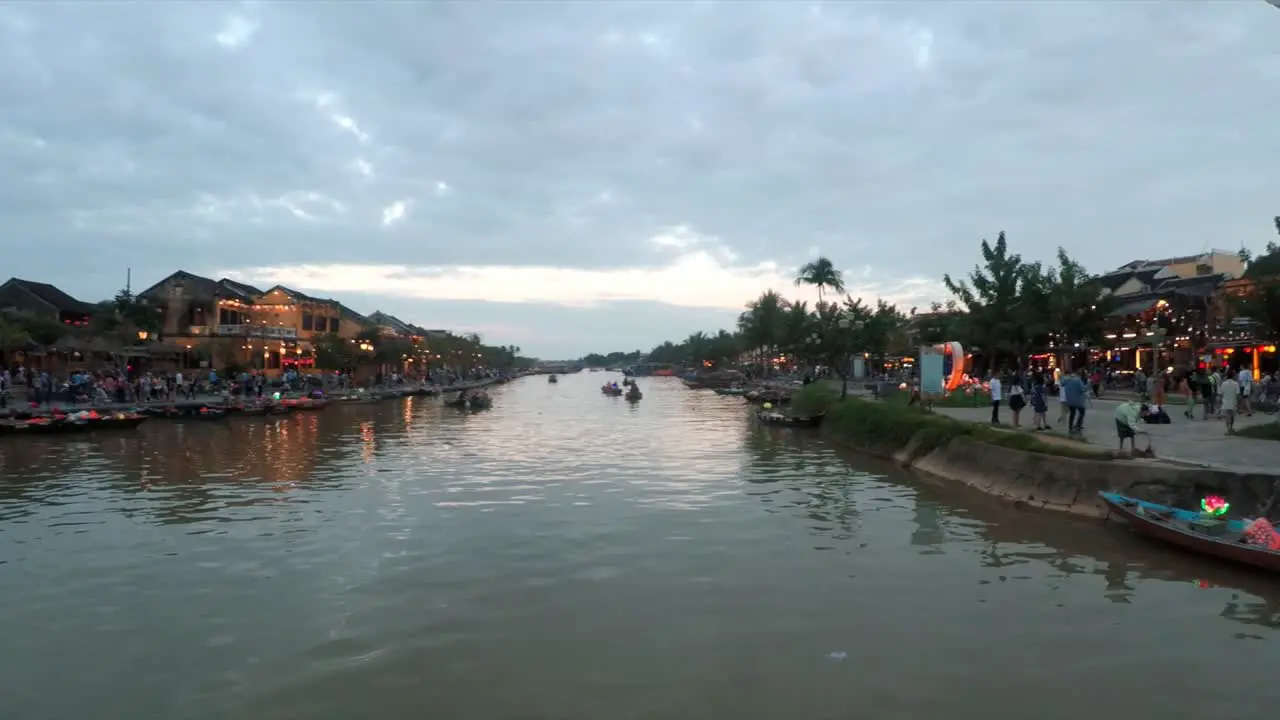 Lanterns by a River with Many People Walking By and Shops Decorated with Lights