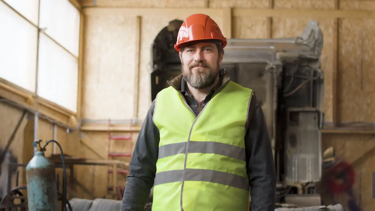 Arbeiter Mit Weste Und Schutzhelm Hält Ein Smartphone In Der Hand Und Blickt In Die Kamera In Einem Logistikpark 1