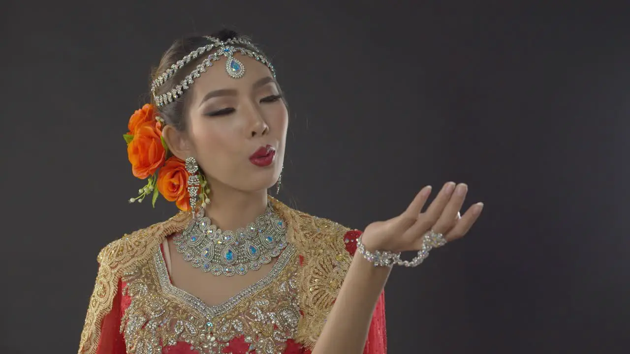 Stunning bride in traditional Indian wedding dress makeup and jewelry blows a kiss to the groom who is out of frame