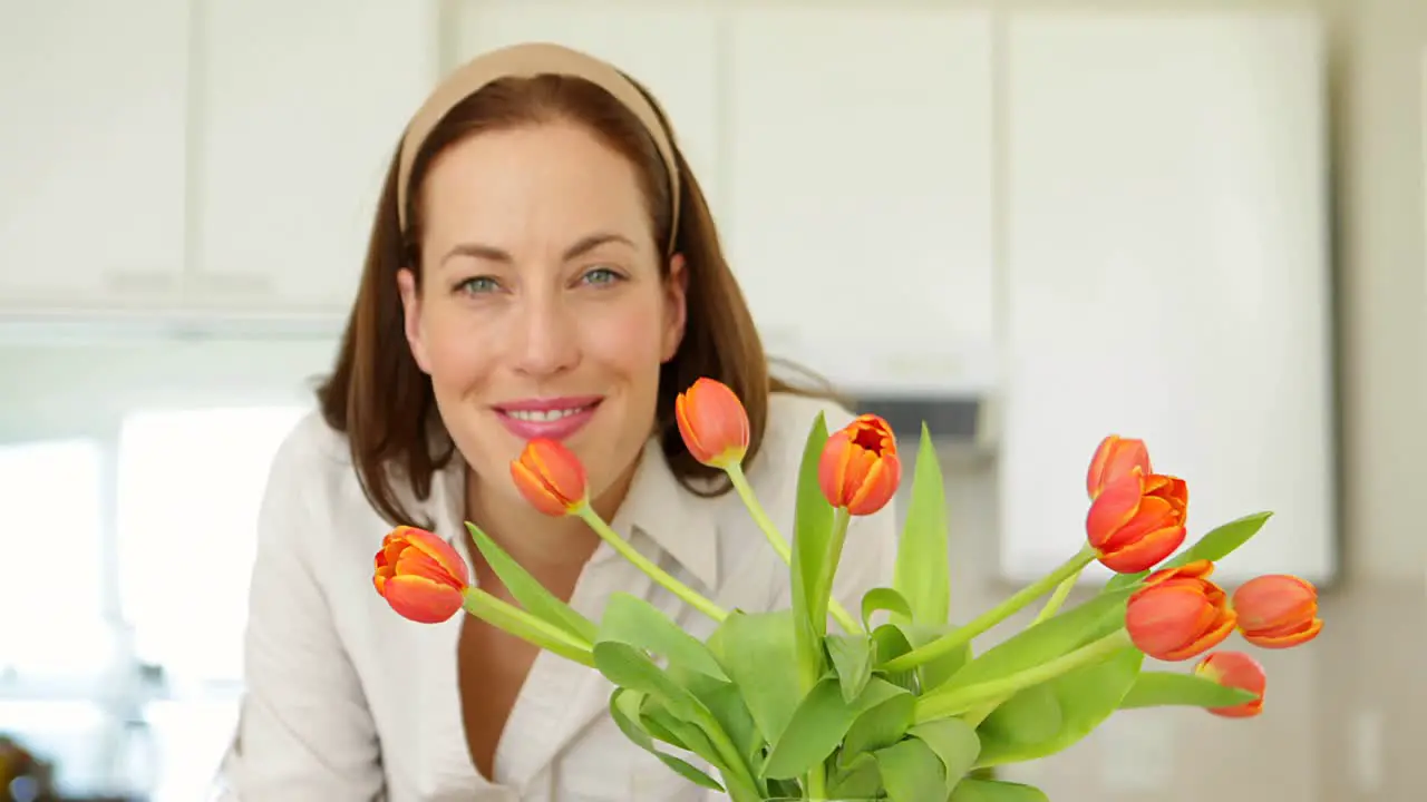 Pretty woman smelling her vase of tulips and smiling at camera