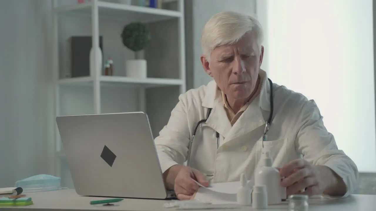 A Grey Haired Middle Aged Doctor Consults On A Notebook The Composition Of A Medicine