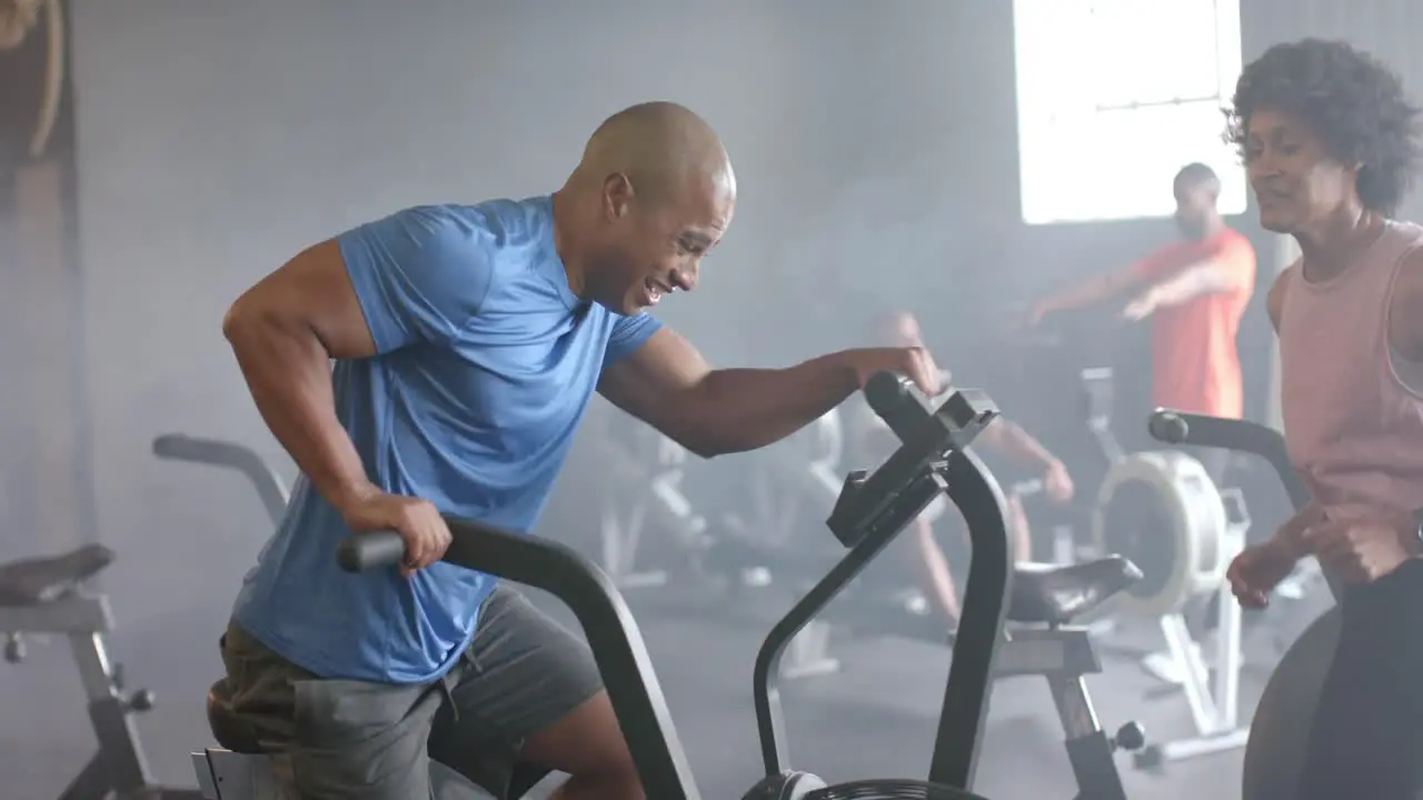 Diverse female coach motivating determined man training hard on elliptical bike at gym slow motion