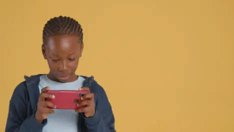 Studio Portrait Of Excited Boy On ASD Spectrum Gaming On Mobile Phone On Yellow Background