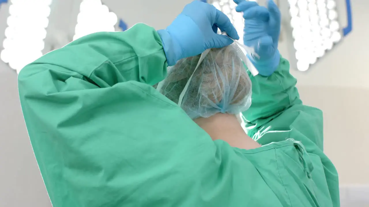 Caucasian female surgeon wearing surgical gown and cap in operating theatre slow motion