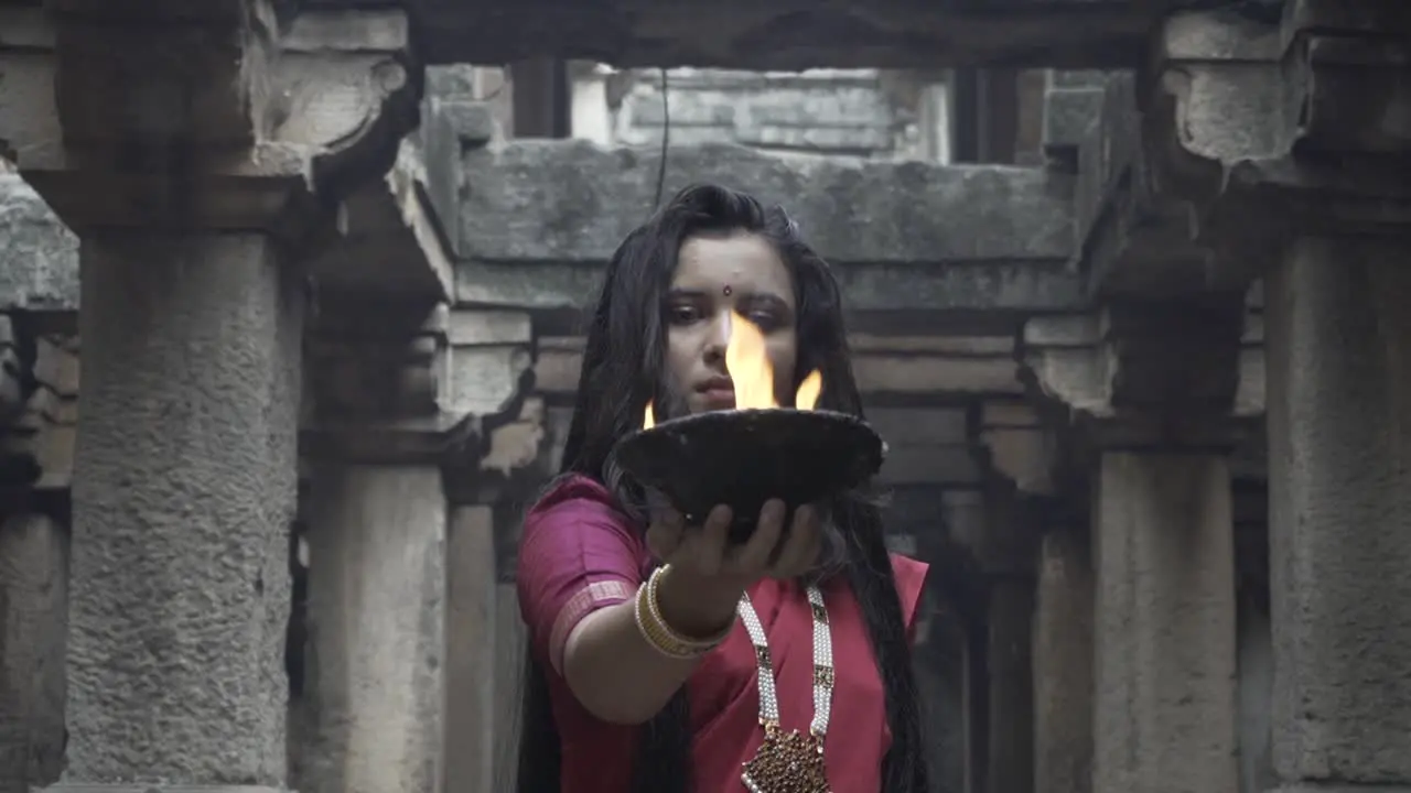 beautiful Indian girl in old stepwell wearing traditional Indian red saree gold jewellery and bangles holding fire plate