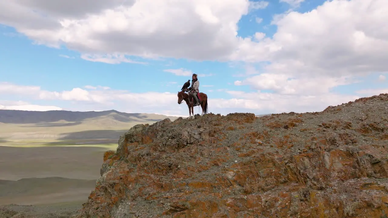 Eagle Hunter With Trained Eagle On A Horse Standing On The Clifftop In Western Mongolia