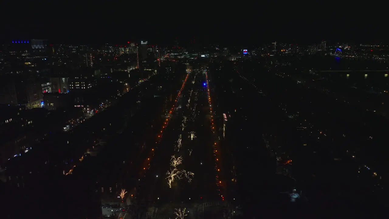 Forwards fly above night city Wide straight street lined by street lights and with illuminated trees in middle Boston USA