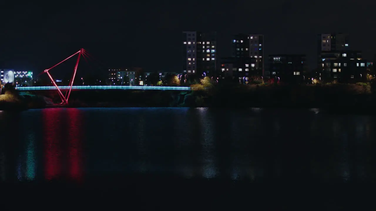 Night view of Pae park pedestrian bridge illuminated with colorful light over lake water with buildings at background Tallinn Estonia