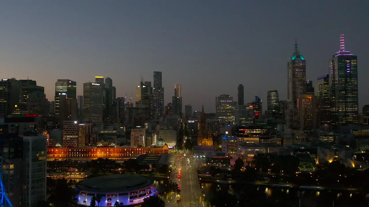 Dusk tracking aerial perspective moving down St Kilda Road toward Melbourne Art Spire and Flinders Street Station