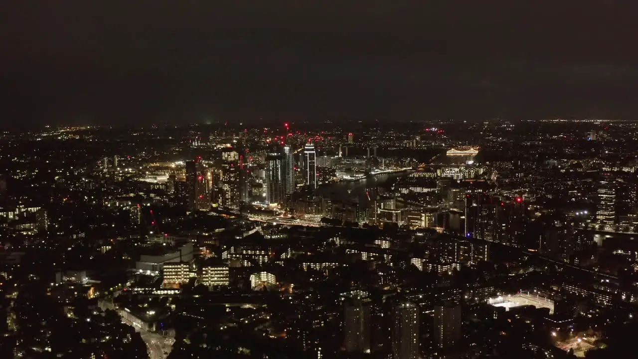 Aerial panoramic view of large city at night City lights glowing into dark Fly above urban neighbourhood London UK