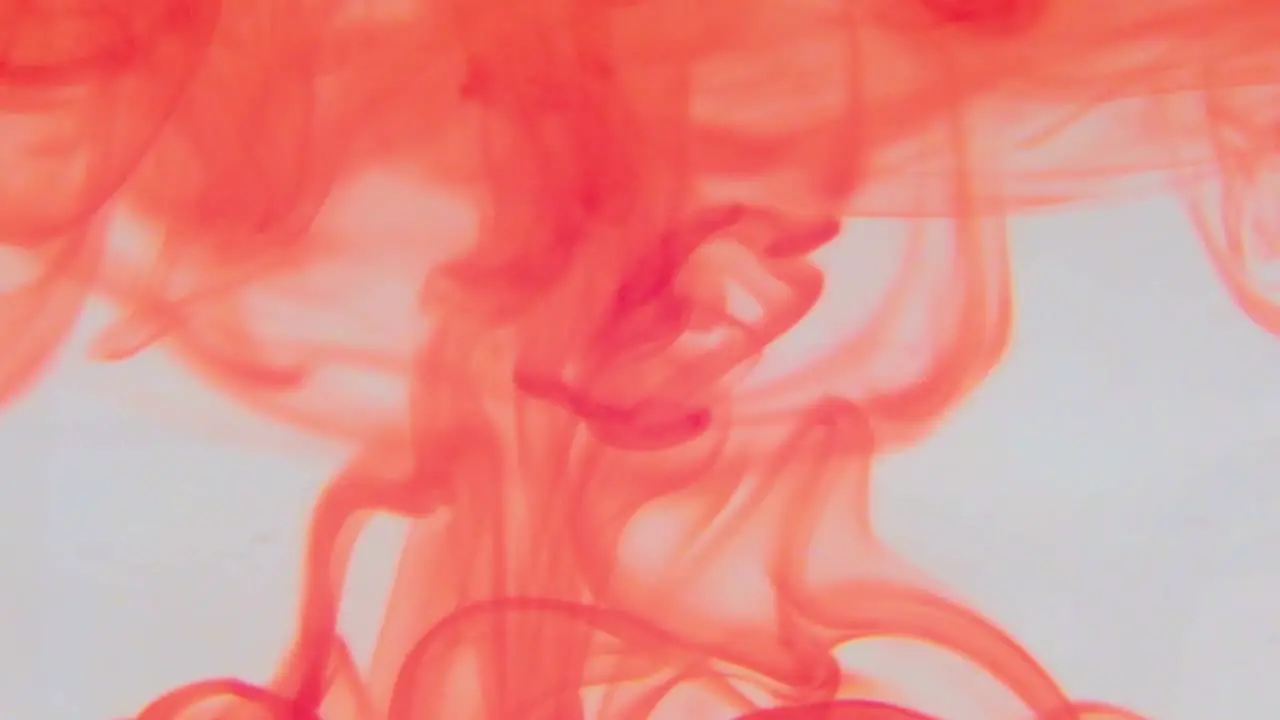 Red food coloring swirling in a container of water 