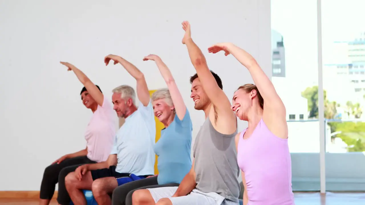 Fitness group sitting on exercise balls stretching arms