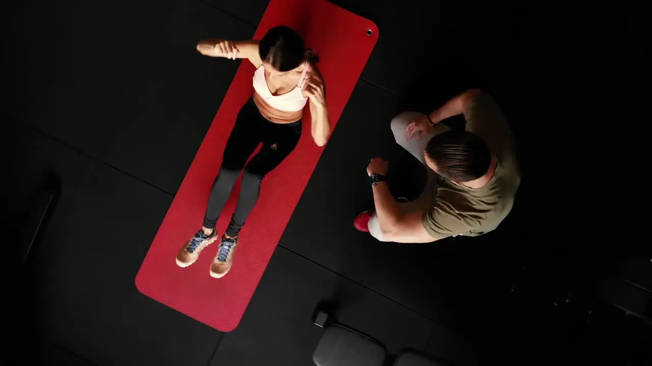 Top down rotating drone shot of sporty woman exercising on mat with personal trainer