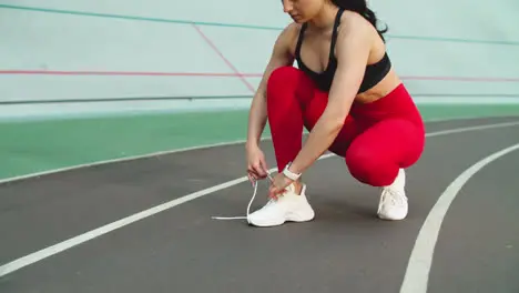 Woman runner preparing for workout on track Fitness girl tying up shoes outdoor