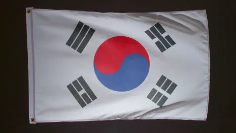 Studio Shot Of Flag Of South Korea Falling Down Against Black Background