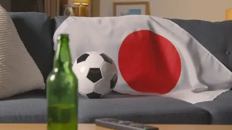 Flag Of Japan Draped Over Sofa At Home With Football Ready For Match On TV