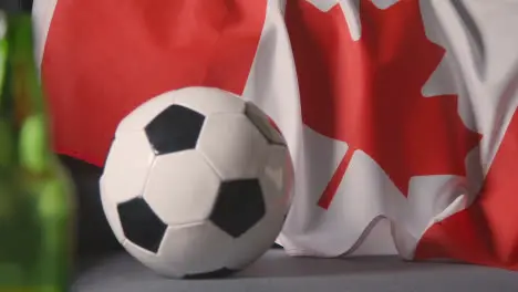 Flag Of Canada Draped Over Sofa At Home With Football Ready For Match On TV 2