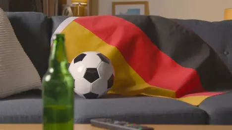 Flag Of Germany Draped Over Sofa At Home With Football Ready For Match On TV