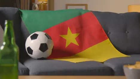 Flag Of Cameroon Draped Over Sofa At Home With Football Ready For Match On TV