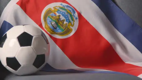 Close Up Of Flag Of Costa Rica Draped Over Sofa At Home With Football Ready For Match On TV