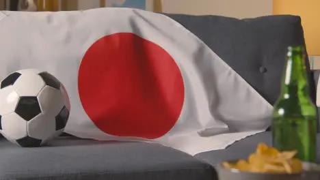 Flag Of Japan Draped Over Sofa At Home With Football Ready For Match On TV 1