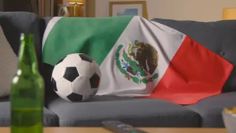 Flag Of Mexico Draped Over Sofa At Home With Football Ready For Match On TV