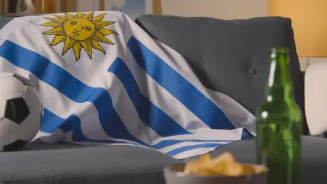 Flag Of Uruguay Draped Over Sofa At Home With Football Ready For Match On TV 1