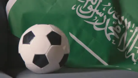 Close Up Of Flag Of Saudi Arabia Draped Over Sofa At Home With Football Ready For Match On TV