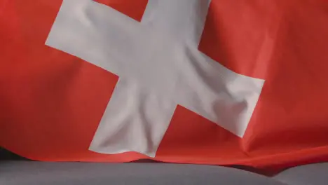 Close Up Of Flag Of Switzerland Draped Over Sofa At Home Ready For Match On TV