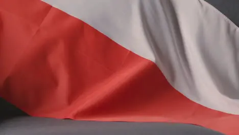 Close Up Of Flag Of Poland Draped Over Sofa At Home With Football Ready For Match On TV